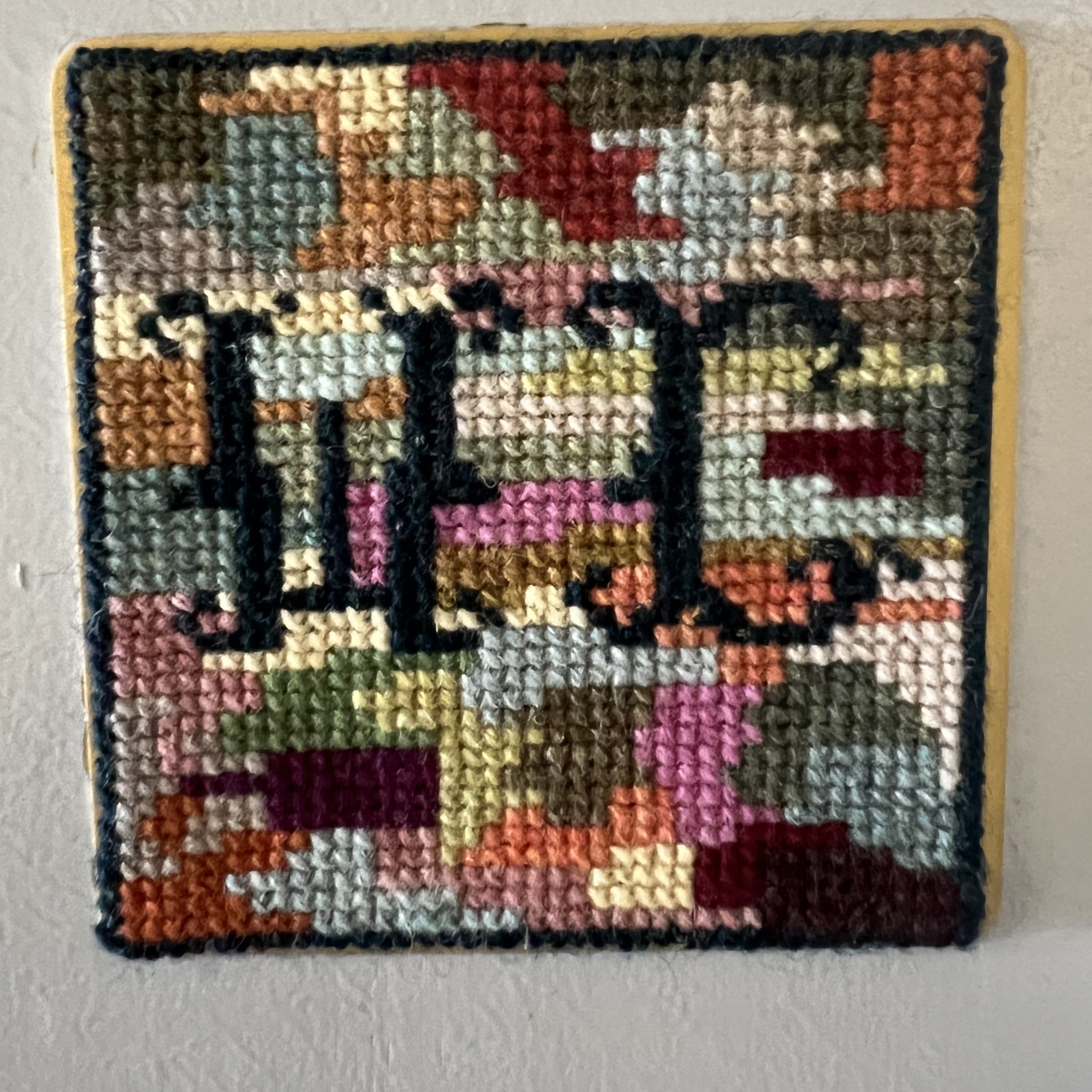 A cross stitched WC sign in warm colors