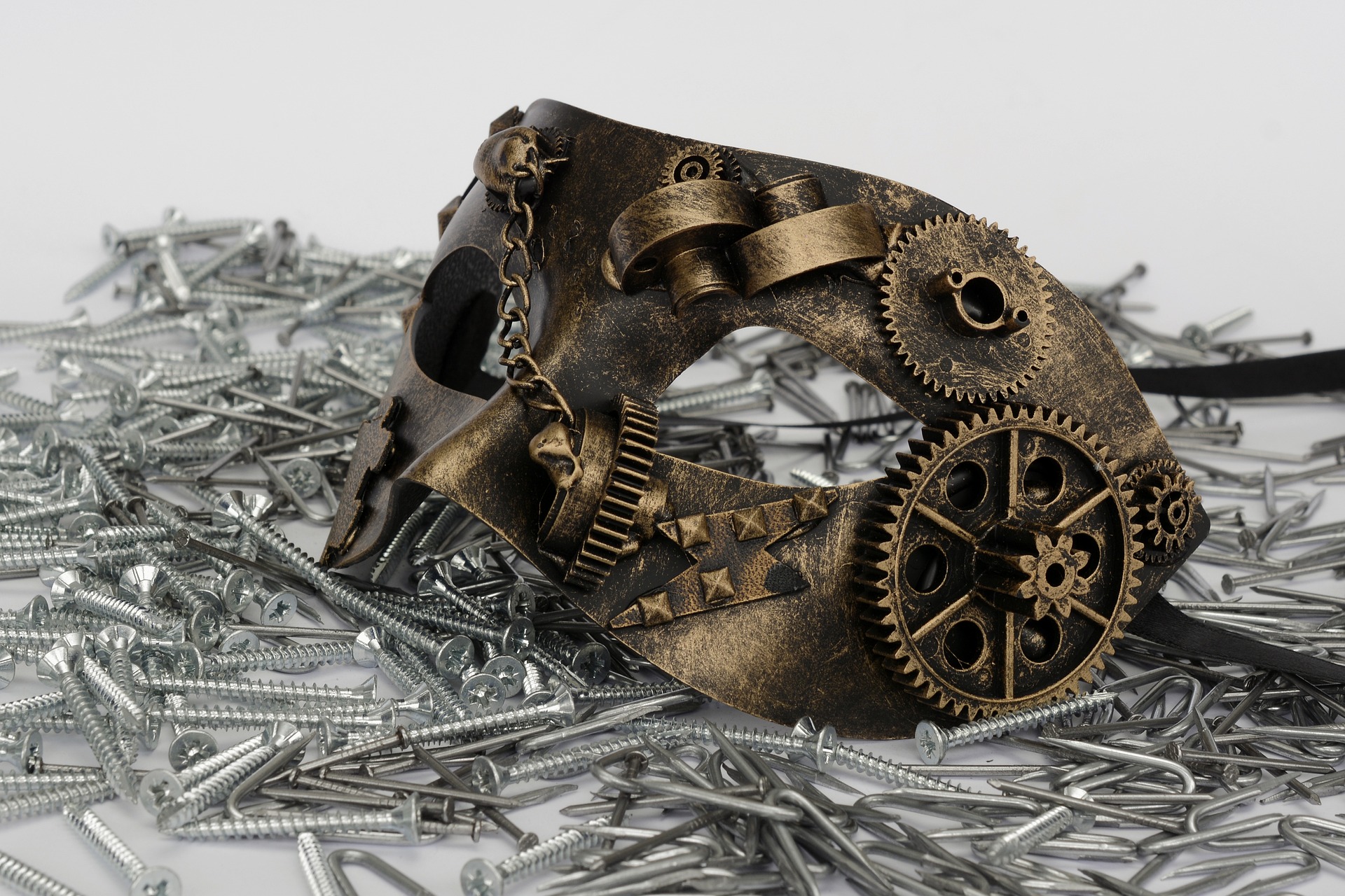 A masquerade mask with cogs and wheels placed on a jumble of screws.